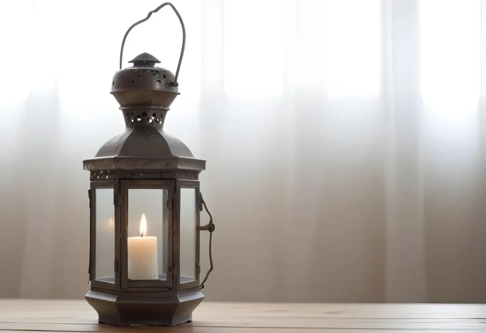 An Antique Metal Lantern With Glass Panels Sits On A Glass Surface A Candle Burning Inside Against A Blurred White Background 21 Ddf0