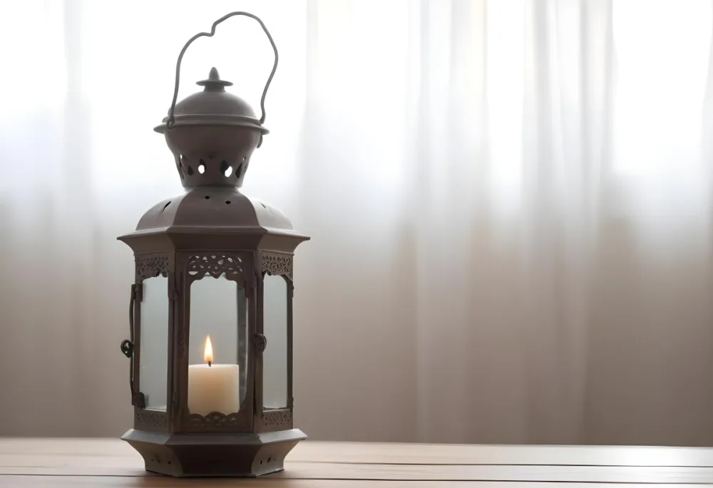 An Antique Metal Lantern With Glass Panels Sits On A Glass Surface A Candle Burning Inside Against A Blurred White Background 23 6843