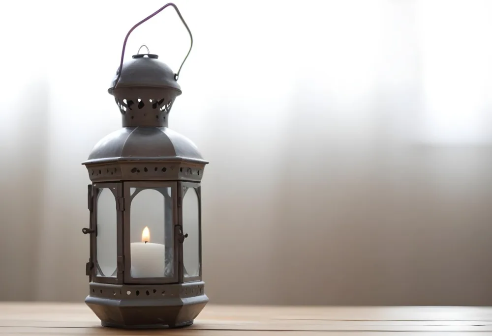 An Antique Metal Lantern With Glass Panels Sits On A Glass Surface A Candle Burning Inside Against A Blurred White Background 3 867c