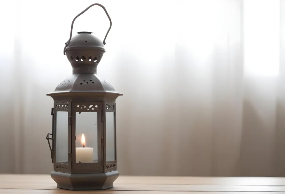 An Antique Metal Lantern With Glass Panels Sits On A Glass Surface A Candle Burning Inside Against A Blurred White Background 33 4dcf