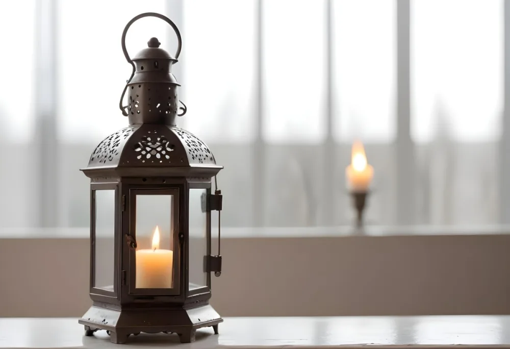 An Antique Metal Lantern With Glass Panels Sits On A Glass Surface A Candle Burning Inside Against A Blurred White Background 4 5f3e