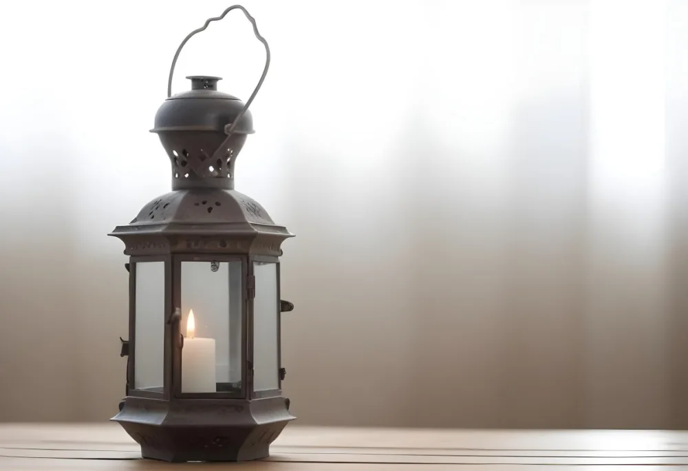 An Antique Metal Lantern With Glass Panels Sits On A Glass Surface A Candle Burning Inside Against A Blurred White Background 5 05c0
