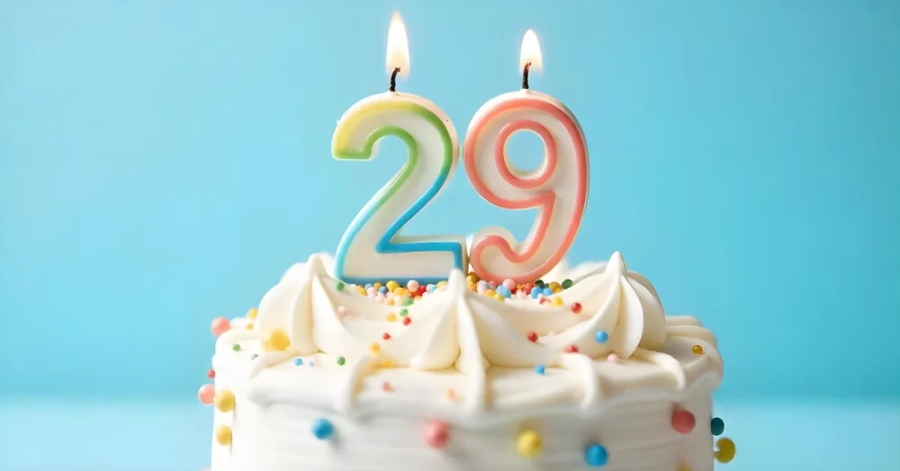 Birthday Cake With White Frosting And Colorful Sprinkles A Candle In The Shape Of The Number 29 Light Blue Background 11 234b