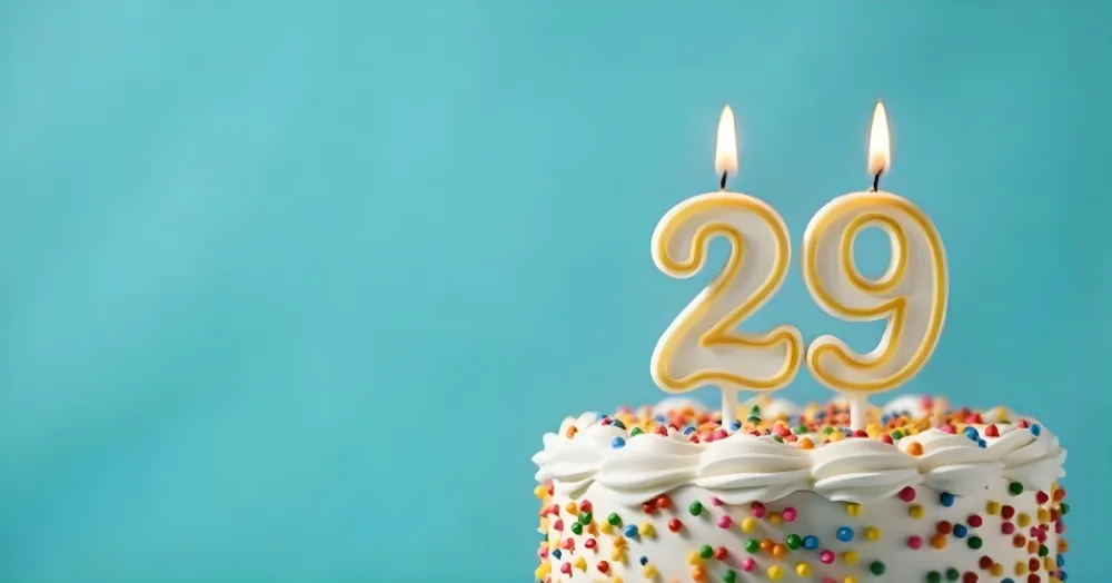 Birthday Cake With White Frosting And Colorful Sprinkles A Candle In The Shape Of The Number 29 Light Blue Background 17 134c