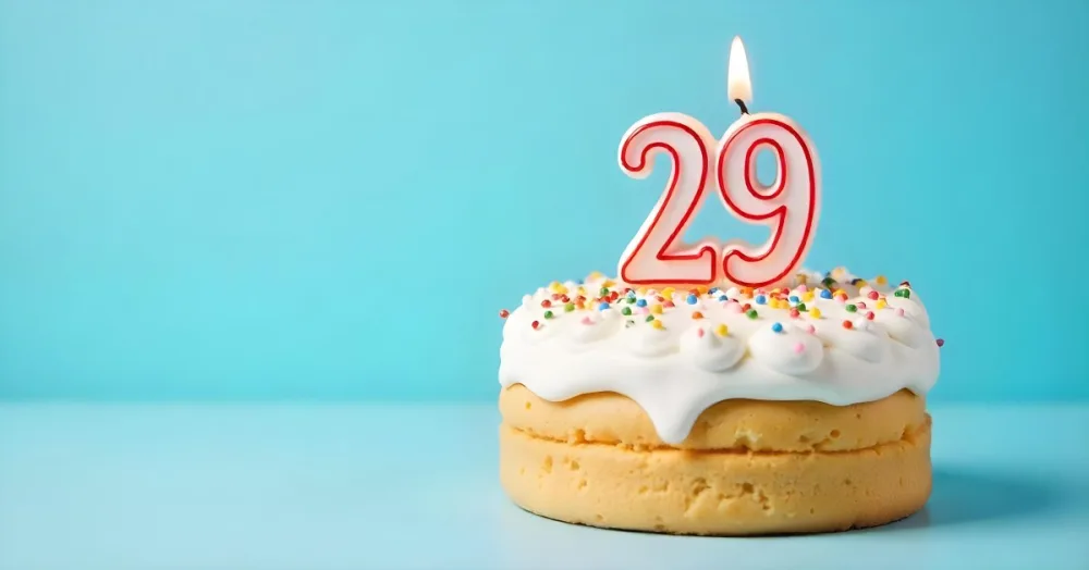 Birthday Cake With White Frosting And Colorful Sprinkles A Candle In The Shape Of The Number 29 Light Blue Background 7 384e