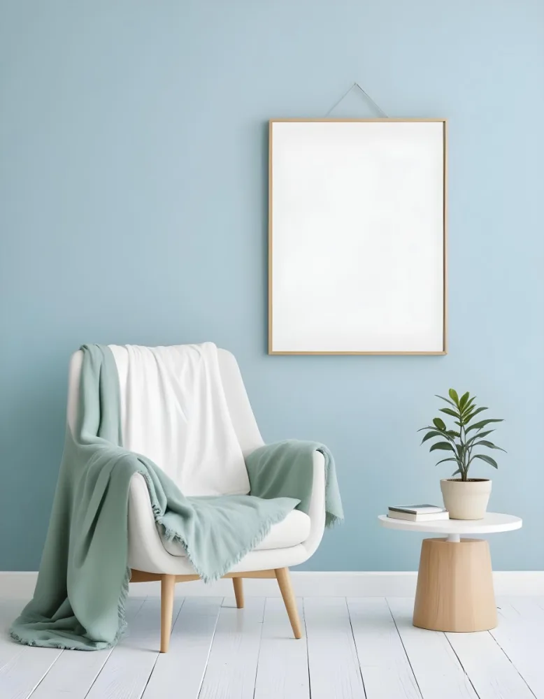 A White Armchair With A Blue Blanket Draped Over It A Small Side Table With A Potted Plant And A Blank White Frame On A Green Wall 17 10b8