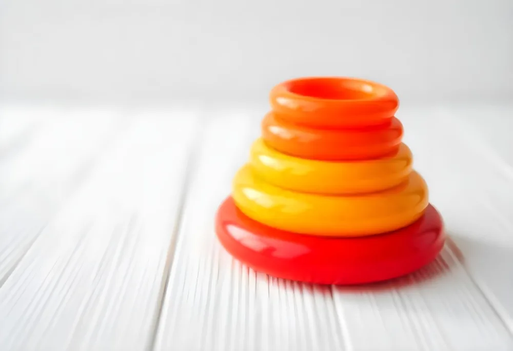 A Red Yellow And Orange Stacking Ring Toy On A White Wooden Surface The Rings Are Plastic And Shiny Close Up Shot 12 C896