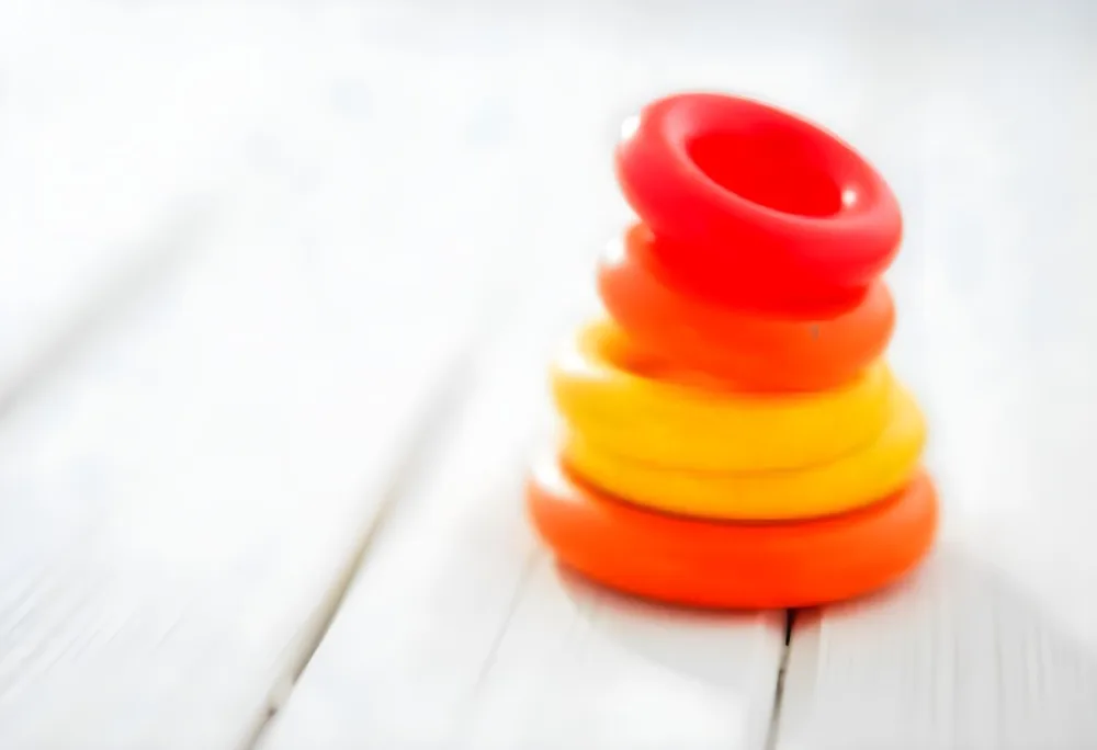 A Red Yellow And Orange Stacking Ring Toy On A White Wooden Surface The Rings Are Plastic And Shiny Close Up Shot 18 C415