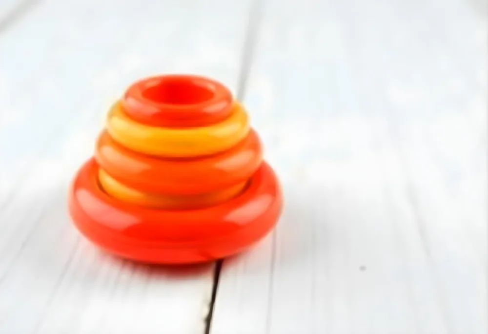 A Red Yellow And Orange Stacking Ring Toy On A White Wooden Surface The Rings Are Plastic And Shiny Close Up Shot 23 44d2