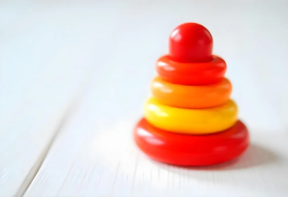 A Red Yellow And Orange Stacking Ring Toy On A White Wooden Surface The Rings Are Plastic And Shiny Close Up Shot 29 56cd