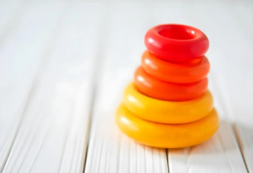 A Red Yellow And Orange Stacking Ring Toy On A White Wooden Surface The Rings Are Plastic And Shiny Close Up Shot 35 F54d