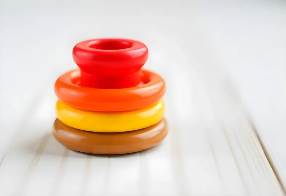 A Red Yellow And Orange Stacking Ring Toy On A White Wooden Surface The Rings Are Plastic And Shiny Close Up Shot 39 7b84
