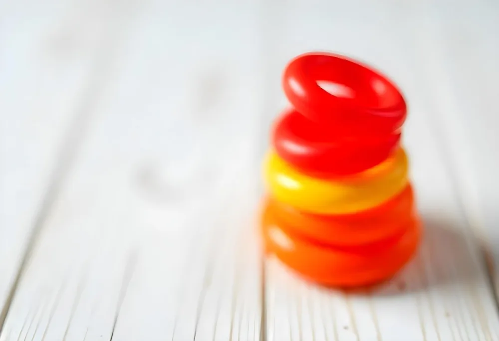 A Red Yellow And Orange Stacking Ring Toy On A White Wooden Surface The Rings Are Plastic And Shiny Close Up Shot 4 99e4