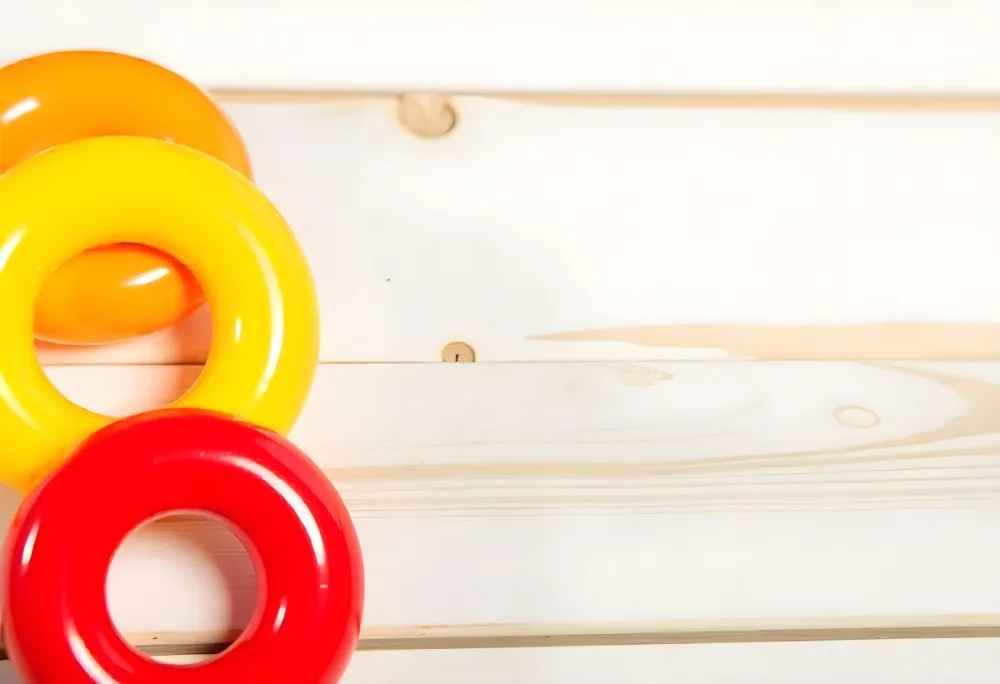 A Red Yellow And Orange Stacking Ring Toy On A White Wooden Surface The Rings Are Plastic And Shiny Close Up Shot 40 175a