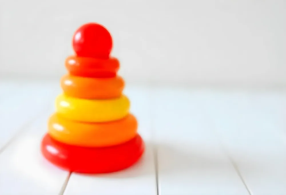 A Red Yellow And Orange Stacking Ring Toy On A White Wooden Surface The Rings Are Plastic And Shiny Close Up Shot 41 Eeb2