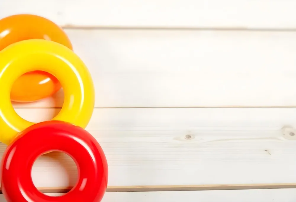 A Red Yellow And Orange Stacking Ring Toy On A White Wooden Surface The Rings Are Plastic And Shiny Close Up Shot 42 B812