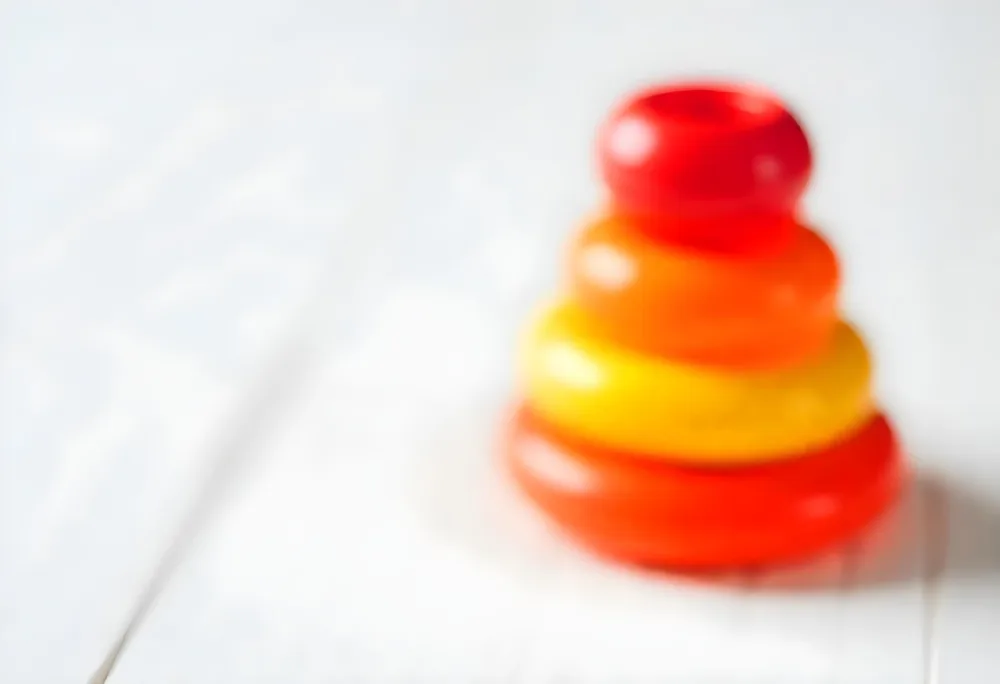 A Red Yellow And Orange Stacking Ring Toy On A White Wooden Surface The Rings Are Plastic And Shiny Close Up Shot 43 1571