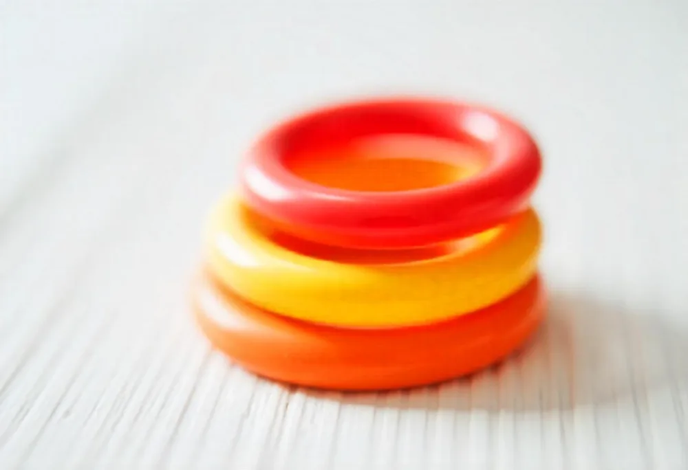 A Red Yellow And Orange Stacking Ring Toy On A White Wooden Surface The Rings Are Plastic And Shiny Close Up Shot 44 D780