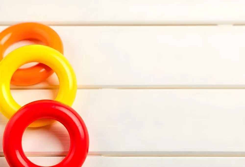 A Red Yellow And Orange Stacking Ring Toy On A White Wooden Surface The Rings Are Plastic And Shiny Close Up Shot 47 B64a