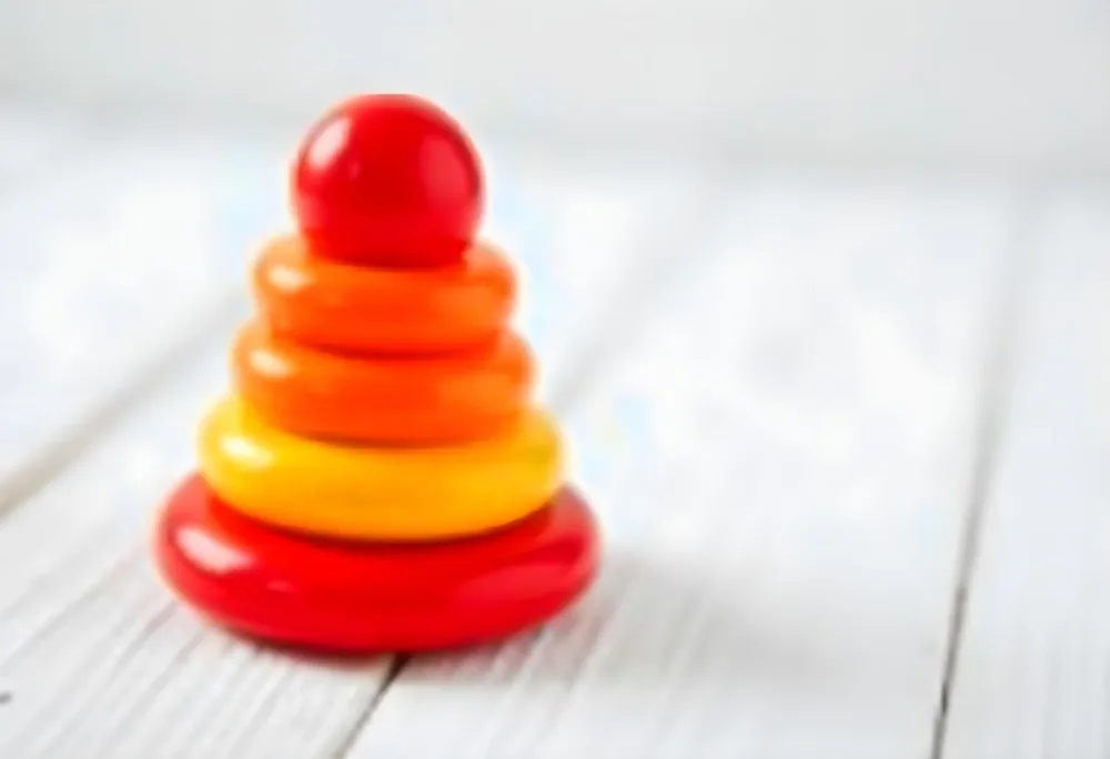 A Red Yellow And Orange Stacking Ring Toy On A White Wooden Surface The Rings Are Plastic And Shiny Close Up Shot 5 2690