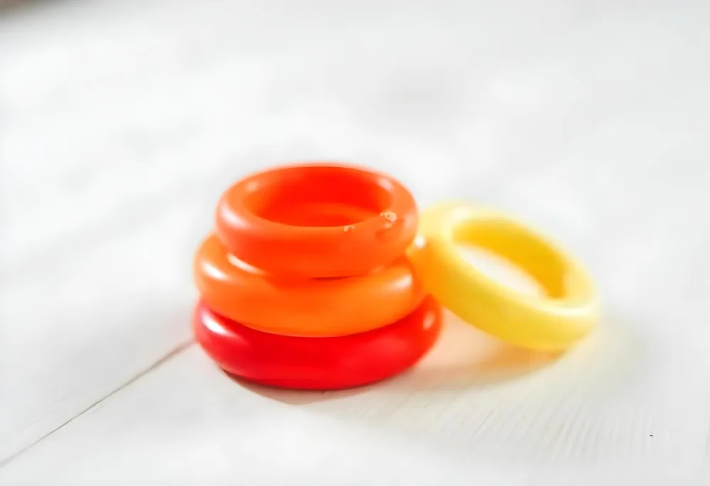 A Red Yellow And Orange Stacking Ring Toy On A White Wooden Surface The Rings Are Plastic And Shiny Close Up Shot 8 Fb10