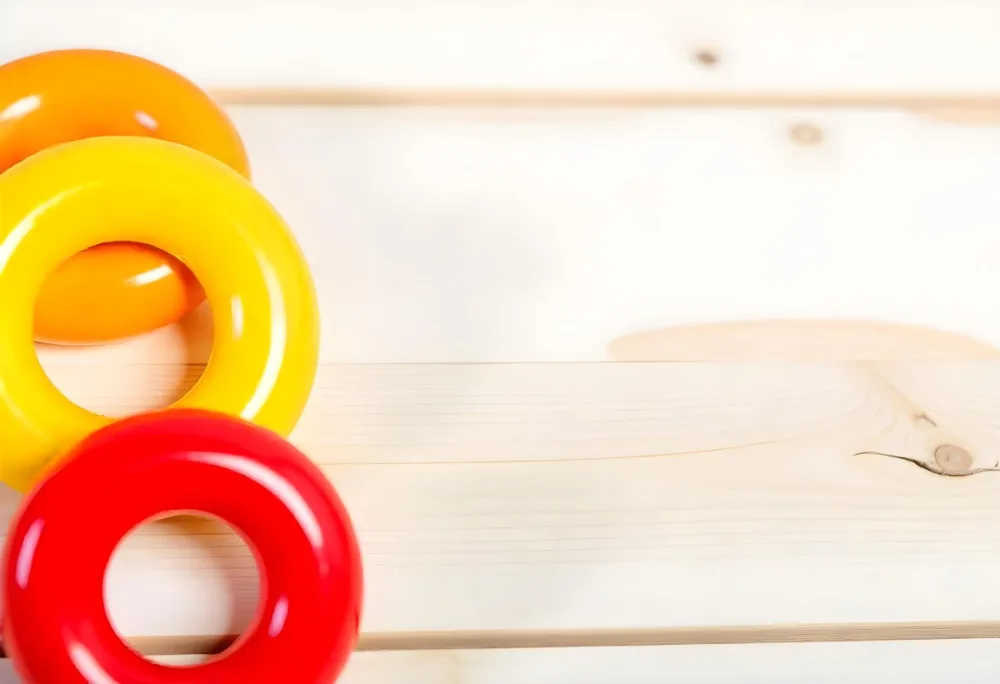 A Red Yellow And Orange Stacking Ring Toy On A White Wooden Surface The Rings Are Plastic And Shiny Close Up Shot 9 C7e5