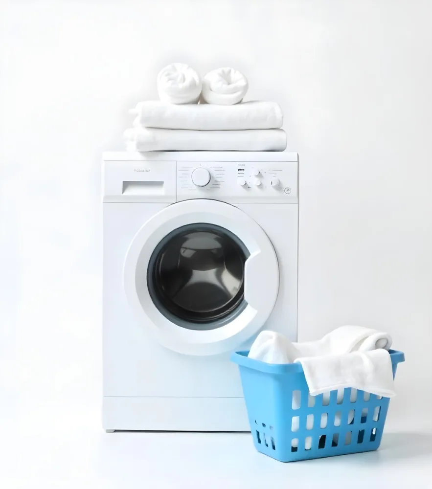 A White Washing Machine With Three White Pillows And Three Towels On Top A Blue Basket With White Clothes On A White Background 16 761c
