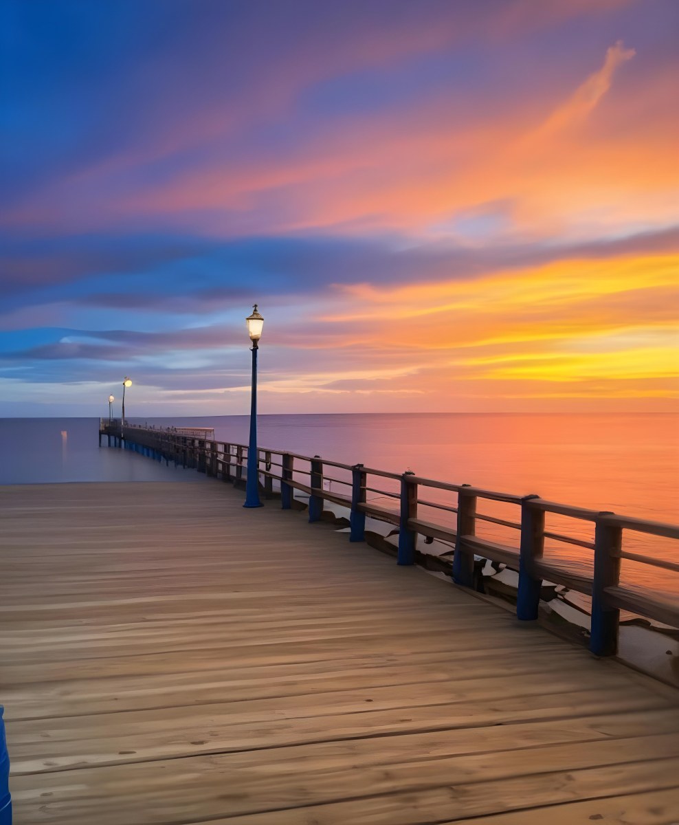 A Wooden Pier With Blue Railings And Lampposts Stretching Into The Ocean At Sunset The Sky Is A Mix Of Orange Pink And Blue 34 F79b