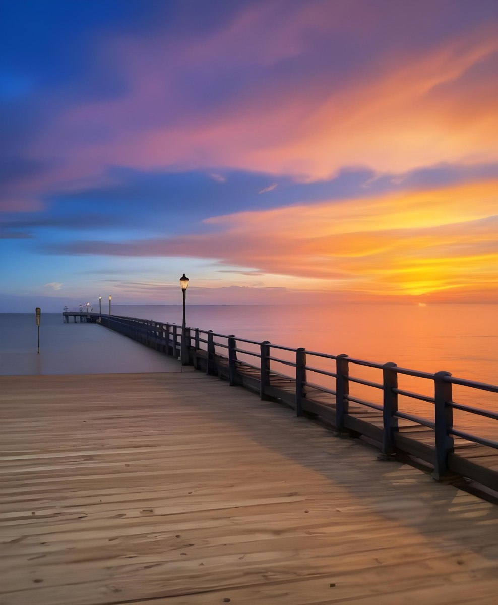A Wooden Pier With Blue Railings And Lampposts Stretching Into The Ocean At Sunset The Sky Is A Mix Of Orange Pink And Blue 46 04ac