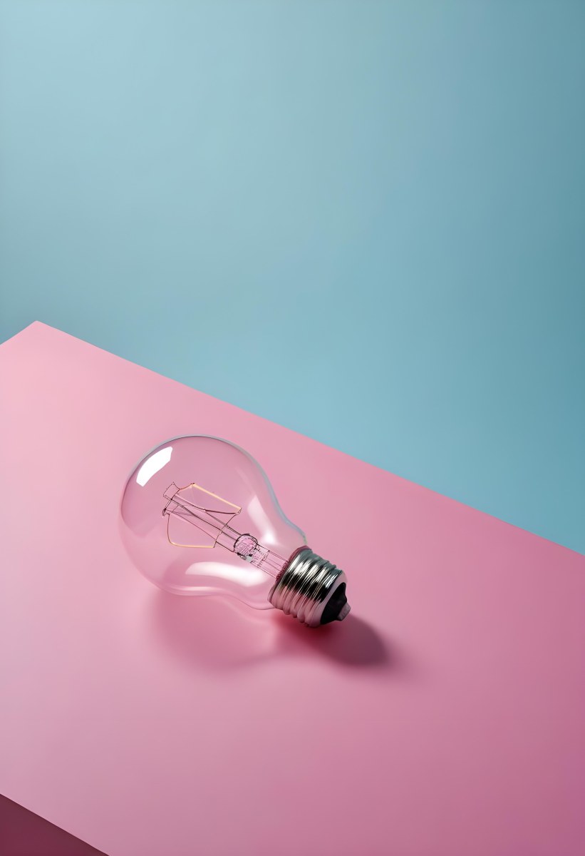 A Clear Light Bulb Lying On A Pink Surface With A Blue Background The Bulb Has A Classic Filament Design Visible Inside The Color Contrast Between The Pink And Blue Creates A Vibrant Aesthetic 25 5e68