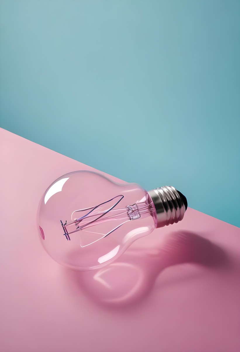 A Clear Light Bulb Lying On A Pink Surface With A Blue Background The Bulb Has A Classic Filament Design Visible Inside The Color Contrast Between The Pink And Blue Creates A Vibrant Aesthetic 27 F7e0