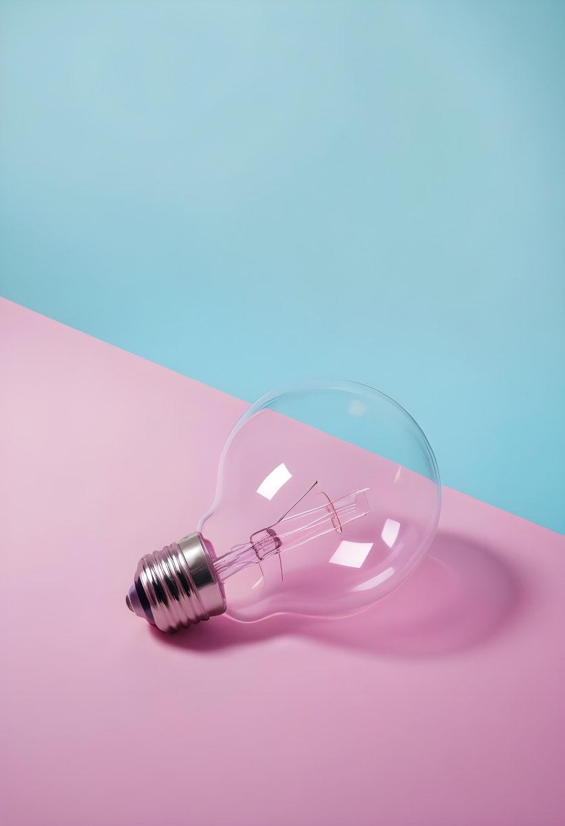 A Clear Light Bulb Lying On A Pink Surface With A Blue Background The Bulb Has A Classic Filament Design Visible Inside The Color Contrast Between The Pink And Blue Creates A Vibrant Aesthetic 30 7cc4