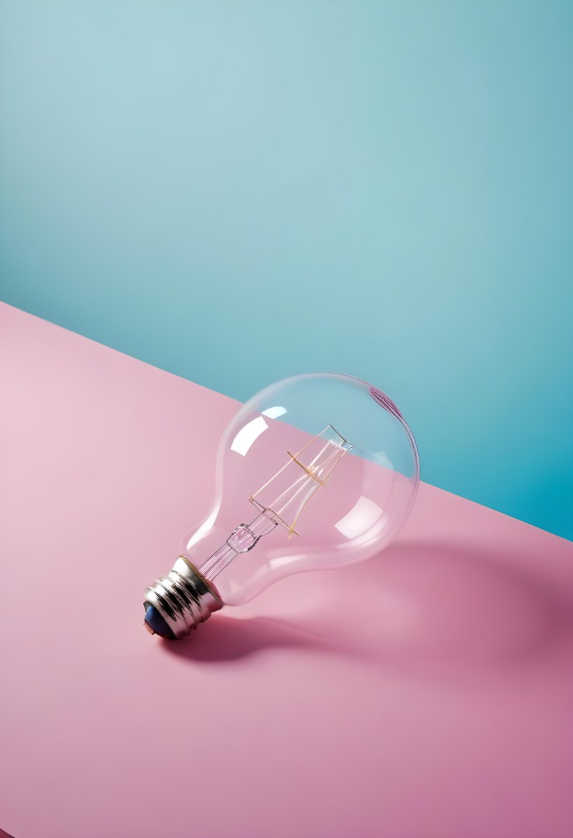 A Clear Light Bulb Lying On A Pink Surface With A Blue Background The Bulb Has A Classic Filament Design Visible Inside The Color Contrast Between The Pink And Blue Creates A Vibrant Aesthetic 31 Bba3