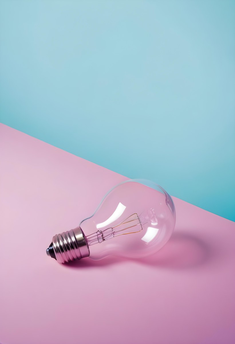 A Clear Light Bulb Lying On A Pink Surface With A Blue Background The Bulb Has A Classic Filament Design Visible Inside The Color Contrast Between The Pink And Blue Creates A Vibrant Aesthetic 36 5ee8