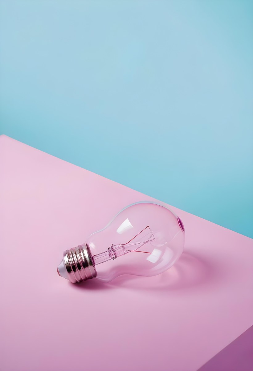 A Clear Light Bulb Lying On A Pink Surface With A Blue Background The Bulb Has A Classic Filament Design Visible Inside The Color Contrast Between The Pink And Blue Creates A Vibrant Aesthetic 4 45a3