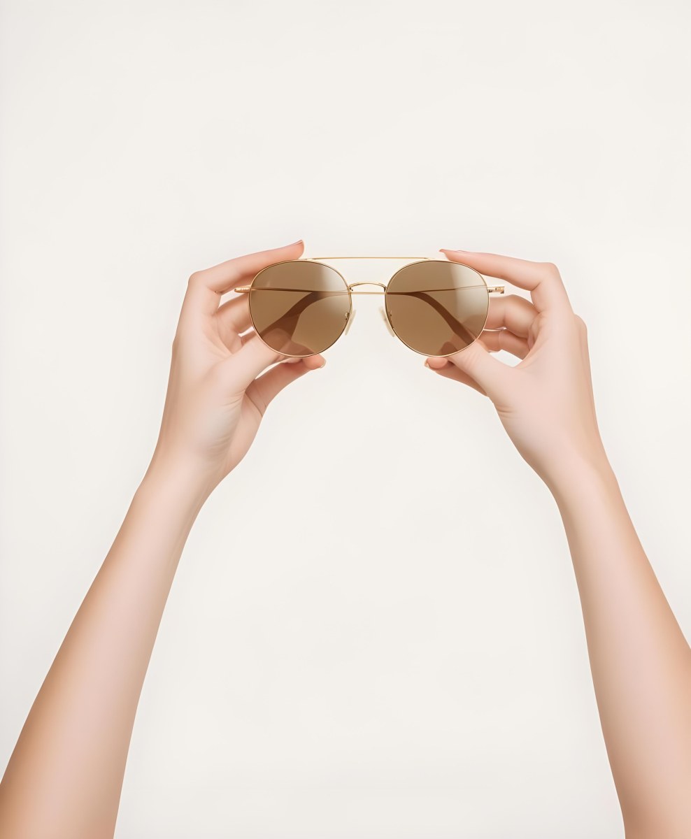 A Woman S Hands Holding A Pair Of Gold Framed Sunglasses Against A Plain White Background 12 6da4