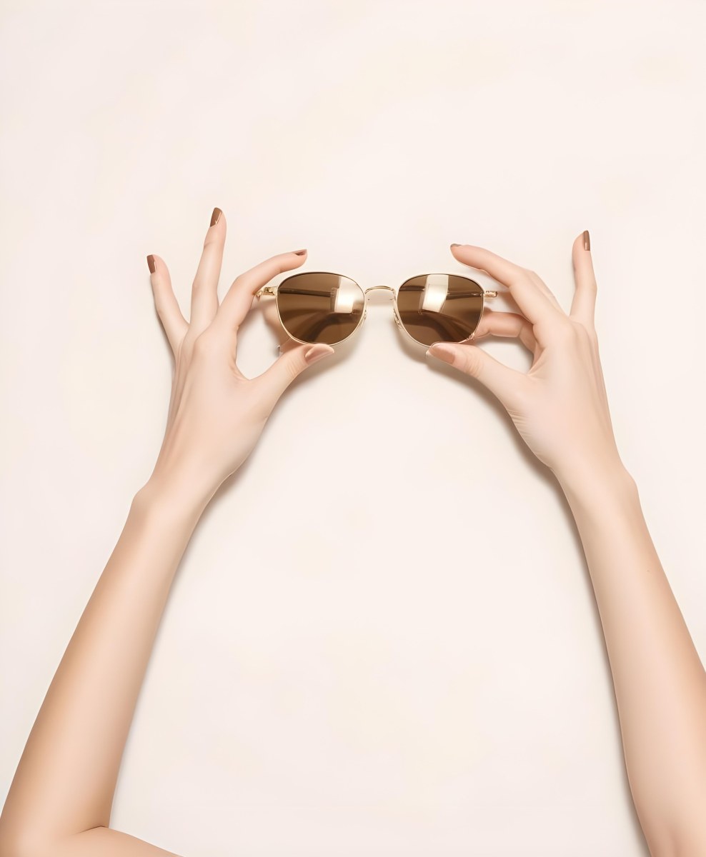 A Woman S Hands Holding A Pair Of Gold Framed Sunglasses Against A Plain White Background 7 B705