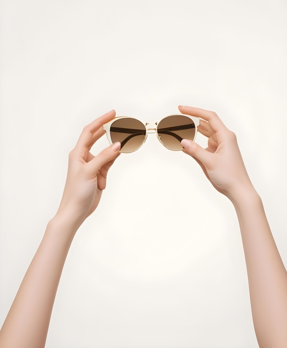 A Woman S Hands Holding A Pair Of Gold Framed Sunglasses Against A Plain White Background 8 0cb6