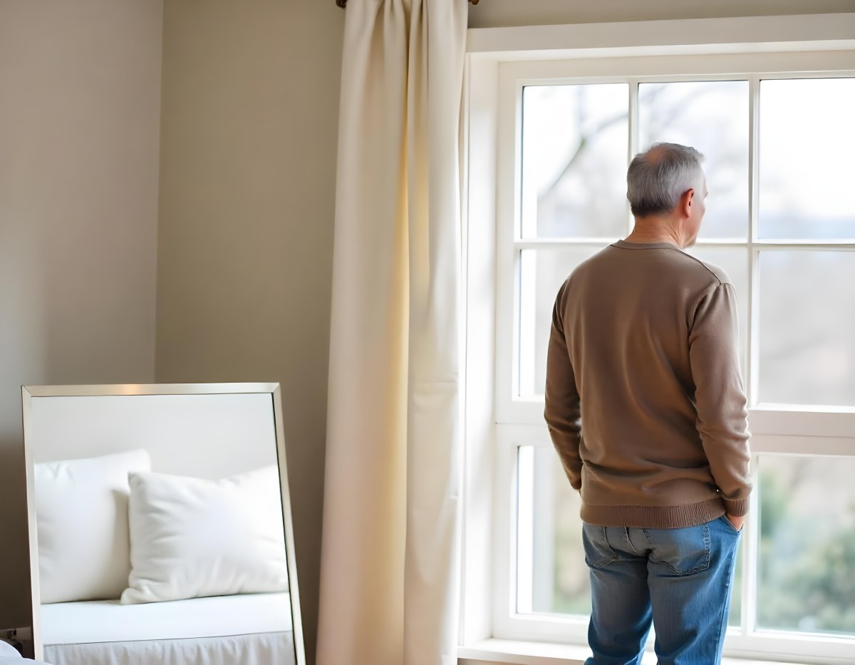 A Middle Aged Caucasian Man With Short Gray Hair Standing By A Window In A Bedroom Looking Outside At A Cityscape During Daytime 11 F791