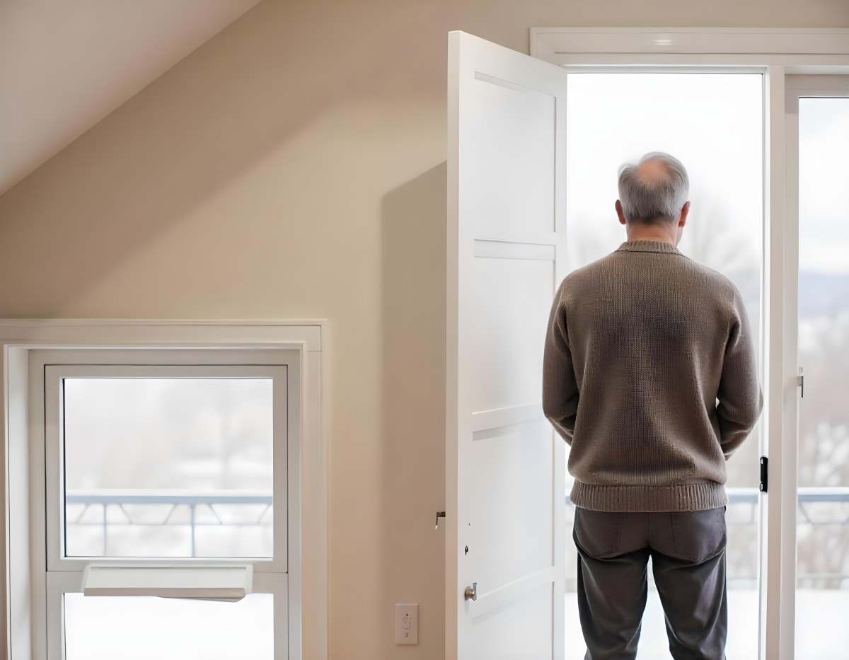 A Middle Aged Caucasian Man With Short Gray Hair Standing By A Window In A Bedroom Looking Outside At A Cityscape During Daytime 13 F864