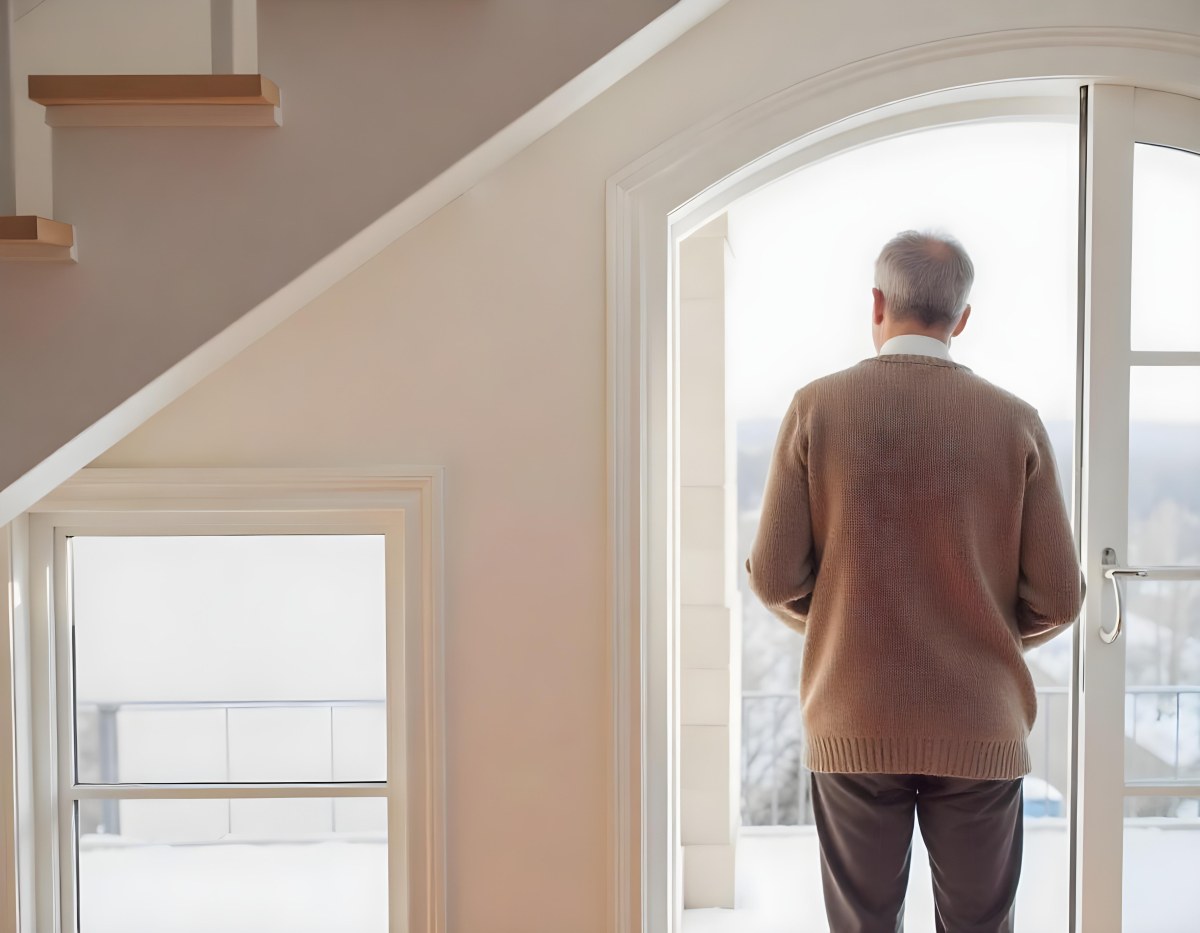 A Middle Aged Caucasian Man With Short Gray Hair Standing By A Window In A Bedroom Looking Outside At A Cityscape During Daytime 14 D04e