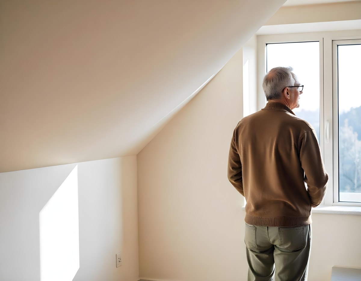 A Middle Aged Caucasian Man With Short Gray Hair Standing By A Window In A Bedroom Looking Outside At A Cityscape During Daytime 16 27a0