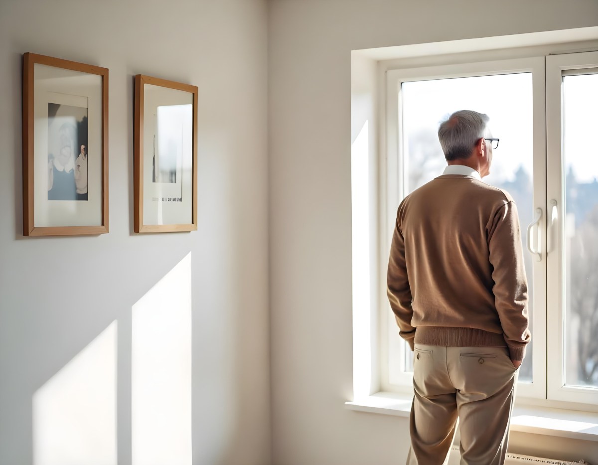 A Middle Aged Caucasian Man With Short Gray Hair Standing By A Window In A Bedroom Looking Outside At A Cityscape During Daytime 4 0c20