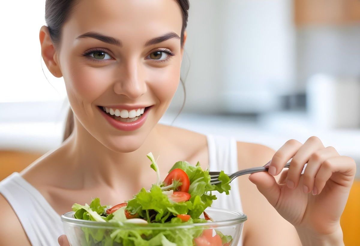 A Young Caucasian Woman With Long Dark Hair Eating A Fresh Green Salad In A Brightly Lit Kitchen Smiling And Looking Down At The Bowl 1 96fd