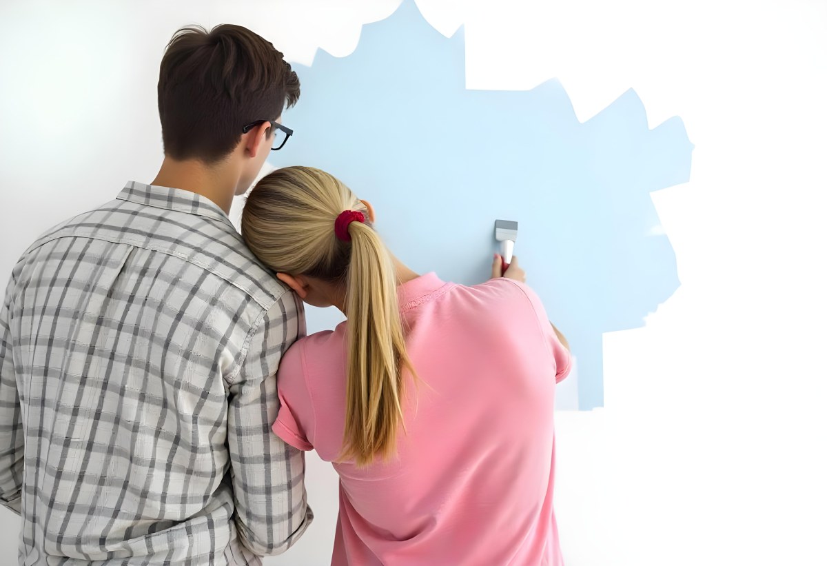 A Young Couple Painting A Wall Together In Their Home The Man Holding A Paint Roller And The Woman Standing Close Behind Her Daytime With Sunlight Streaming In In The Background 8 B2c3