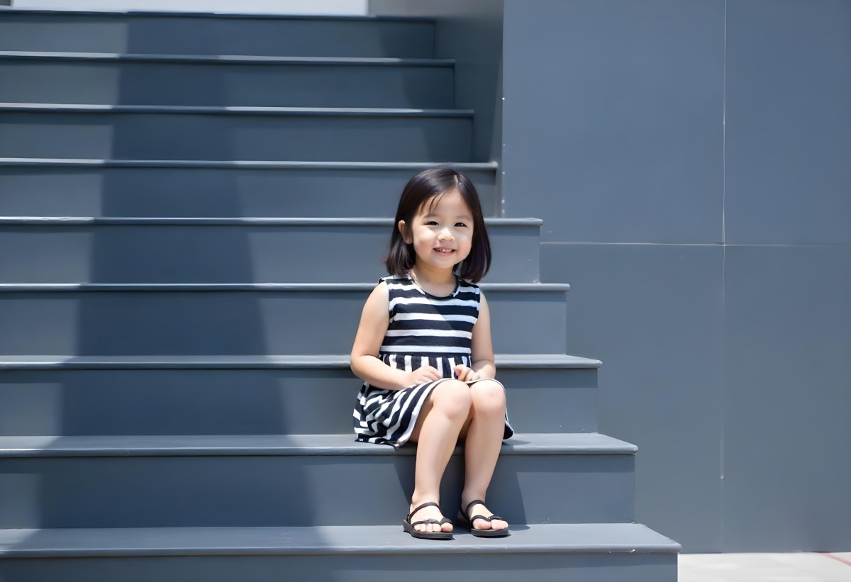 An Asian Girl 6 Years Old Black Hair Sitting On Gray Stairs Wearing A Striped Dress And Black Shoes Gray Background 29 16e9