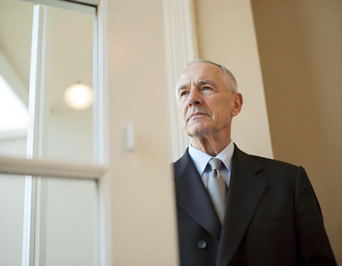 An Elderly Caucasian Man With Gray Hair Wearing A Dark Suit And Tie Standing In Front Of A Window 13 4051