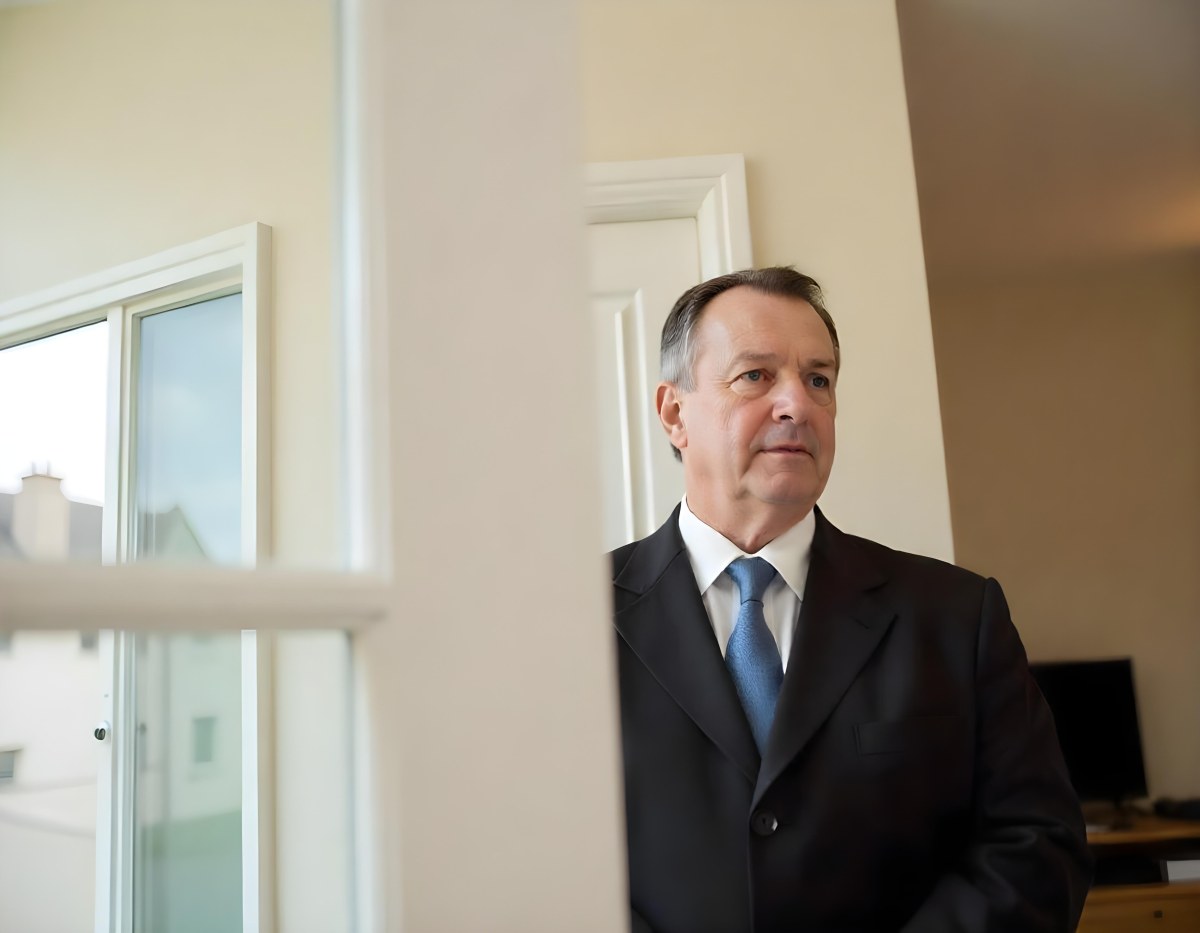 An Elderly Caucasian Man With Gray Hair Wearing A Dark Suit And Tie Standing In Front Of A Window 16 4f19