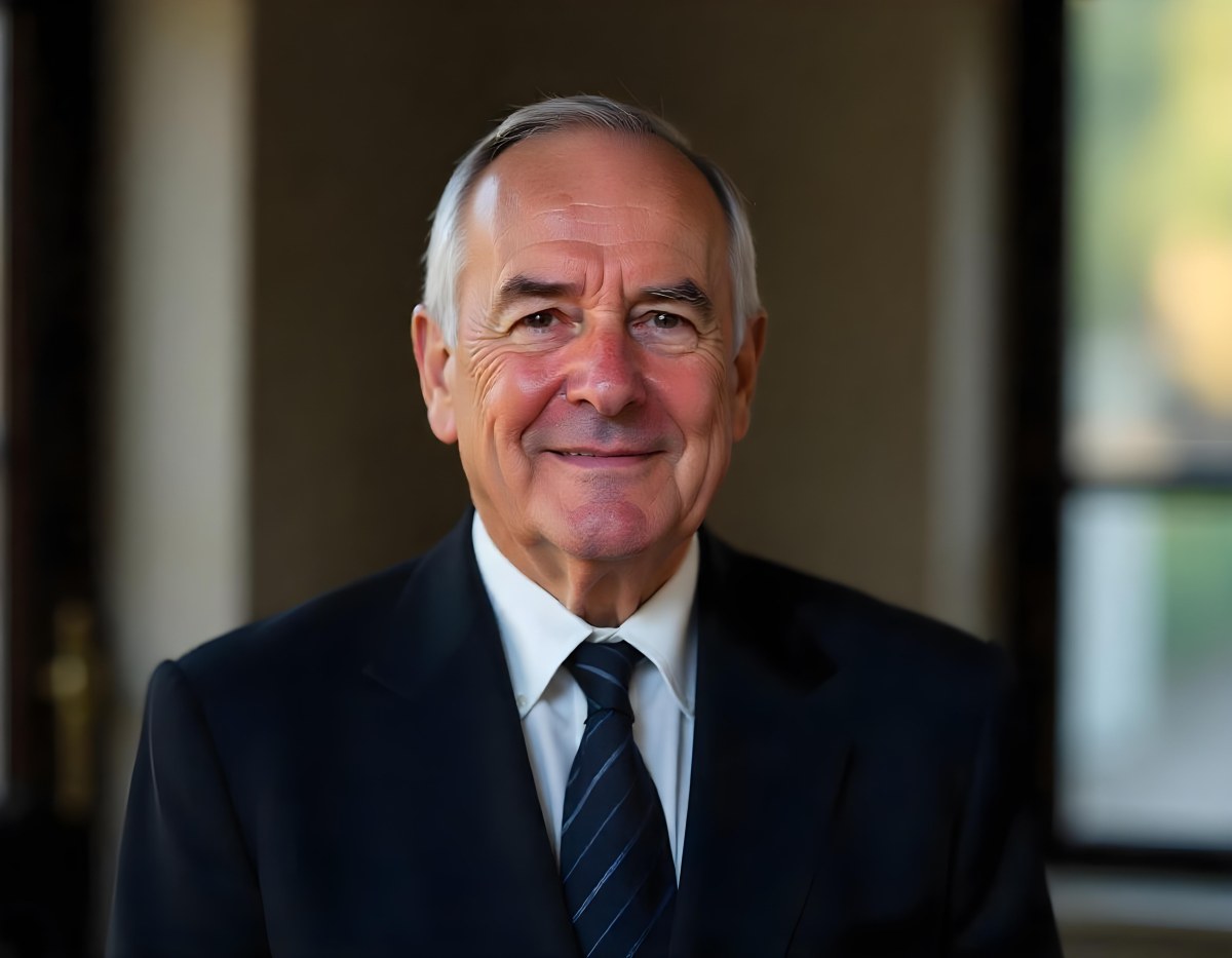 An Elderly Caucasian Man With Gray Hair Wearing A Dark Suit And Tie Standing In Front Of A Window 3 90da