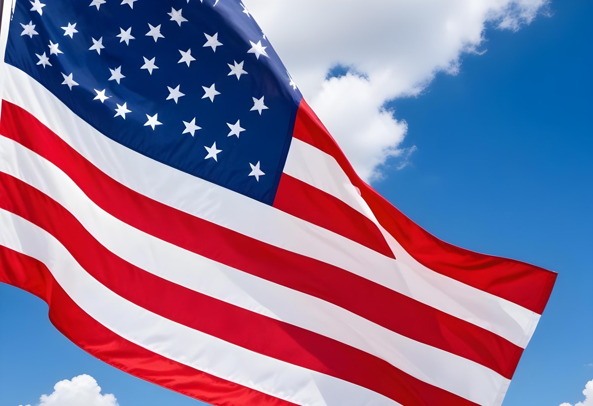 American Flag Waving In The Wind With Its Red And White Stripes And Blue Field Of Stars Against A Blue Sky With White Clouds 17 16b5